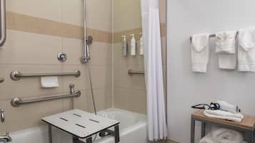 A bathroom with a shower, grab bars, a towel rack, and a small table with towels and a hairdryer.