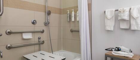 Een badkamer met een douche, handgrepen, een handdoekrek en een klein tafeltje met handdoeken en een haardroger.
