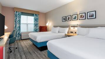A hotel room with two beds, a desk with a chair, a TV, and a window with curtains.