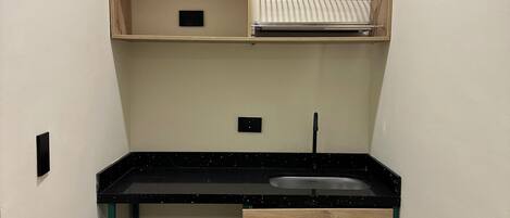 A compact kitchenette with a countertop, a sink, and a wooden cabinet.