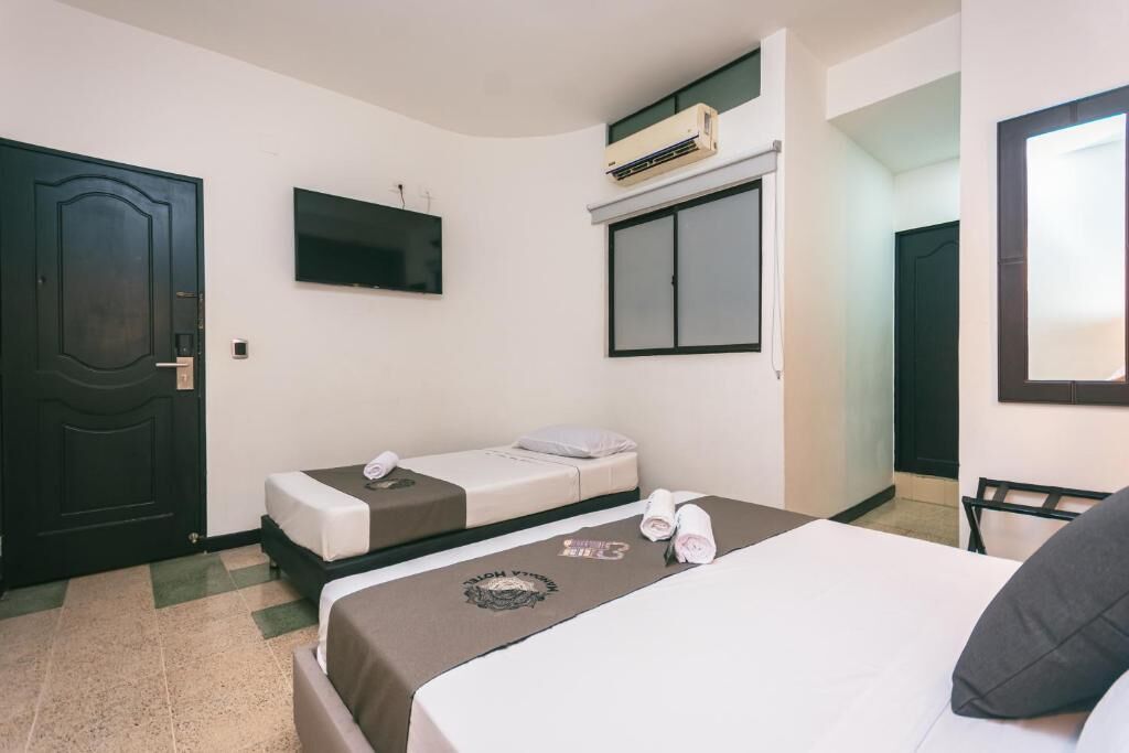 A hotel room with a bed, a smaller bed, a TV, an air conditioning unit, and a door.