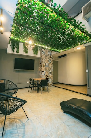 Een modern interieur met een eethoek, zwarte stoelen, een tafel, een aan de muur bevestigde televisie en een decoratieve planteninstallatie.