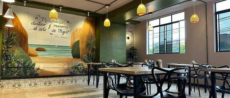 A restaurant with a mural of a beach, tables, chairs, and hanging lights.