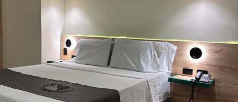 A modern hotel room with a bed, bedside tables, a phone, and a wall-mounted light fixture.