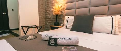 Una habitación de hotel con una cama, una mesita de noche con lámpara, una pequeña mesa y un adorno en la pared.