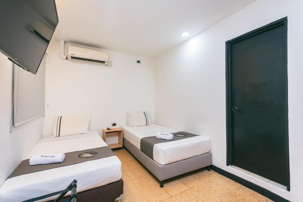A room with two beds, a small bedside table, an air conditioning unit, and a door.