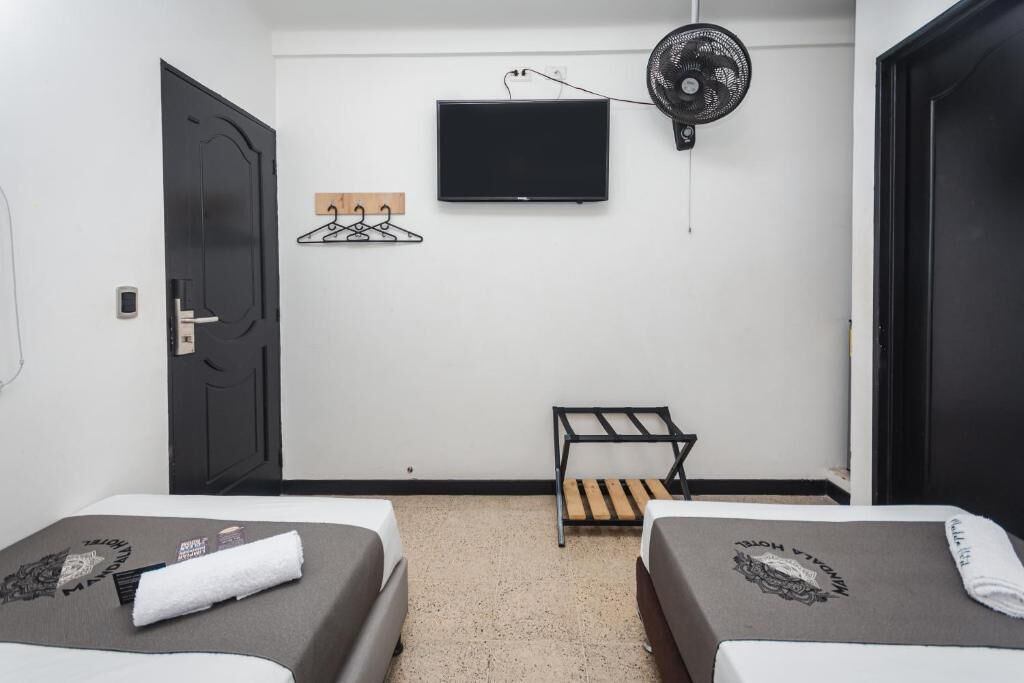 Habitación de hotel con dos camas, televisión, ventilador de pared y perchero.