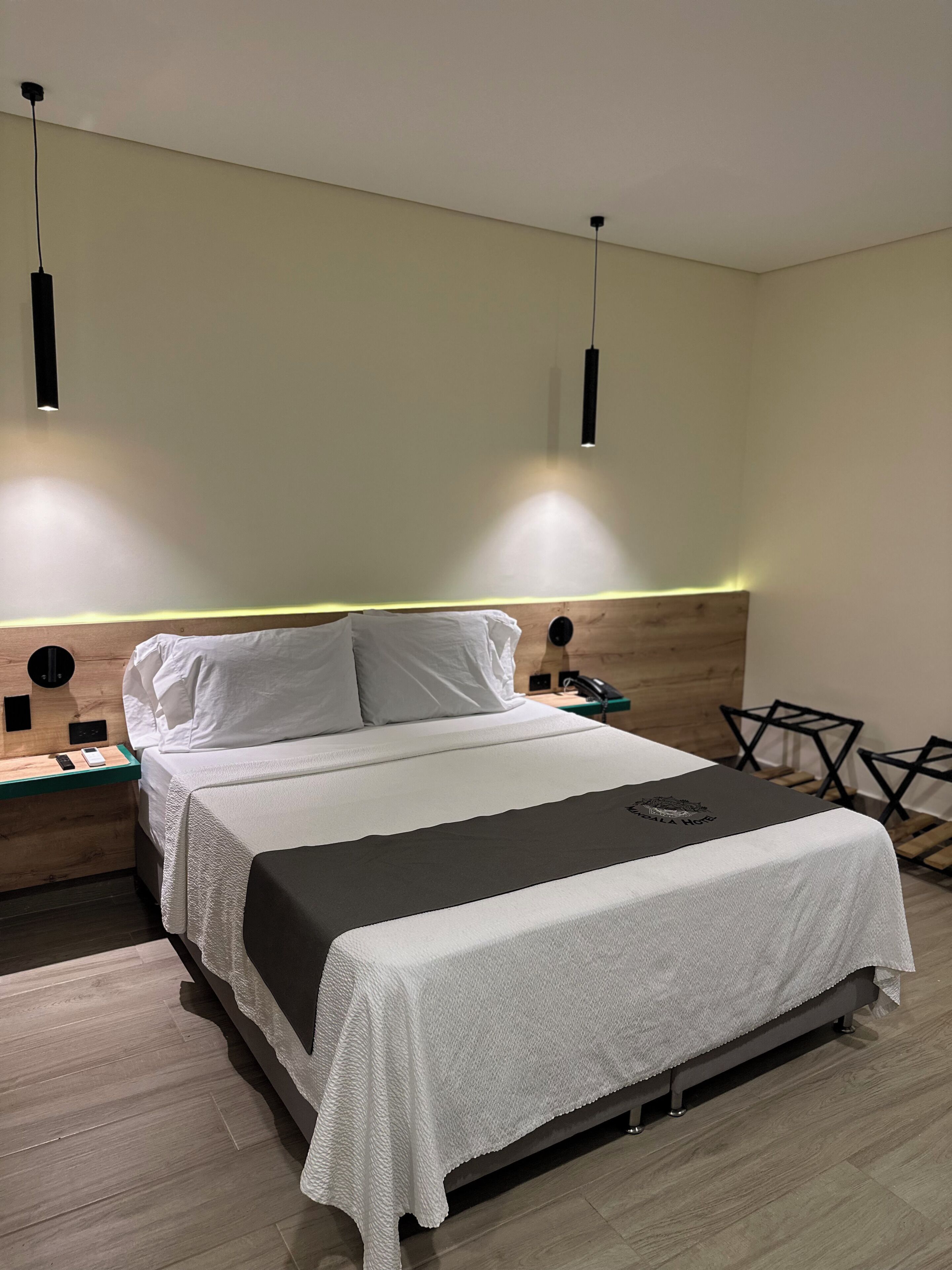 Une chambre d’hôtel moderne avec un lit soigneusement fait, une table de chevet avec une lampe et un petit coin salon avec des fauteuils.