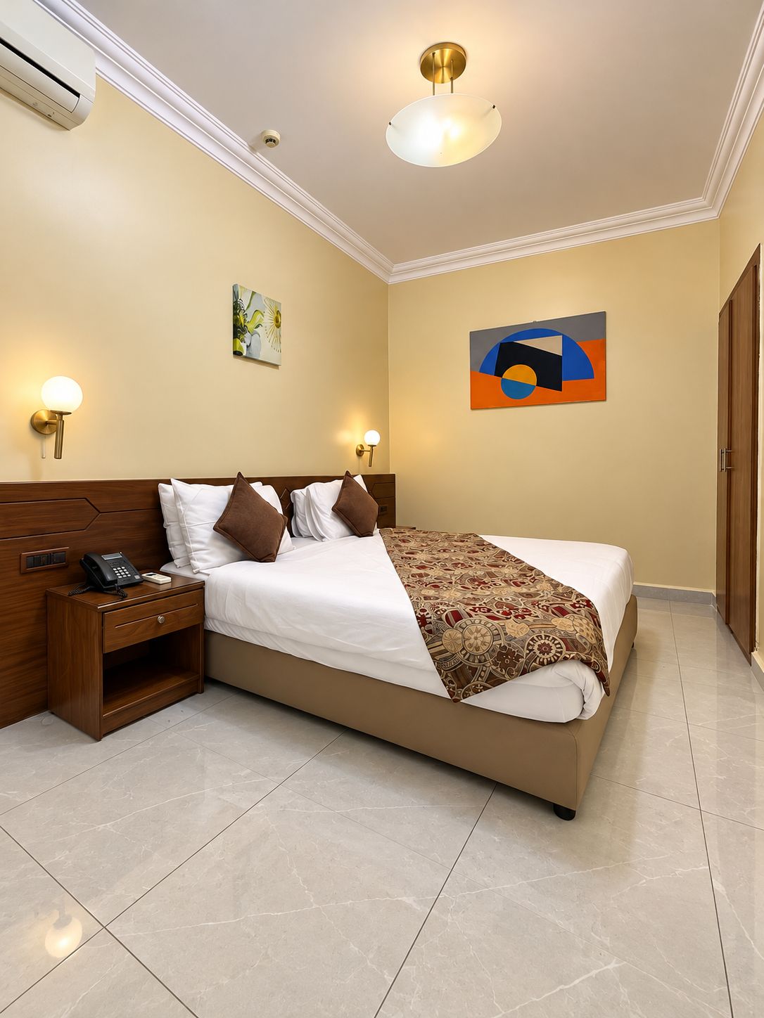 Una habitación de hotel con una cama grande, mesitas de noche, un teléfono y obras de arte en las paredes.