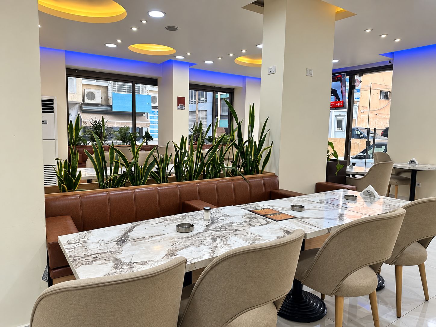 A modern dining area with a marble table, leather booth seating, and potted plants.