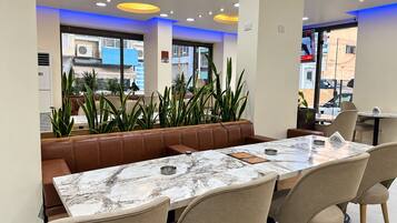 A modern dining area with a marble table, leather booth seating, and potted plants.