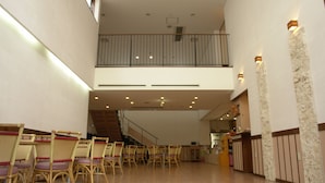 A spacious lobby with a staircase leading to an upper floor, featuring wicker chairs and a reception desk. - Rakuchin Hotel (Naha)