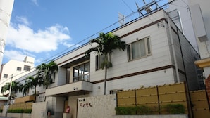 A two-story residential building with a balcony, a small garden, and a wooden fence. - Rakuchin Hotel (Naha)