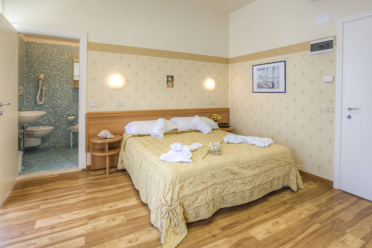 A hotel room with a bed, bedside tables, a bathroom with a sink and toilet, and a door.