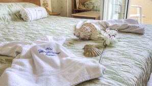 A neatly made bed with a floral-patterned bedspread, a rolled towel, a decorative shell, and a white robe with embroidered text. - San Francisco Spiaggia (Rimini)