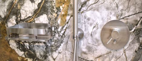 A bathroom with a marble wall, a shower with a handheld showerhead, and a round, metallic control panel.