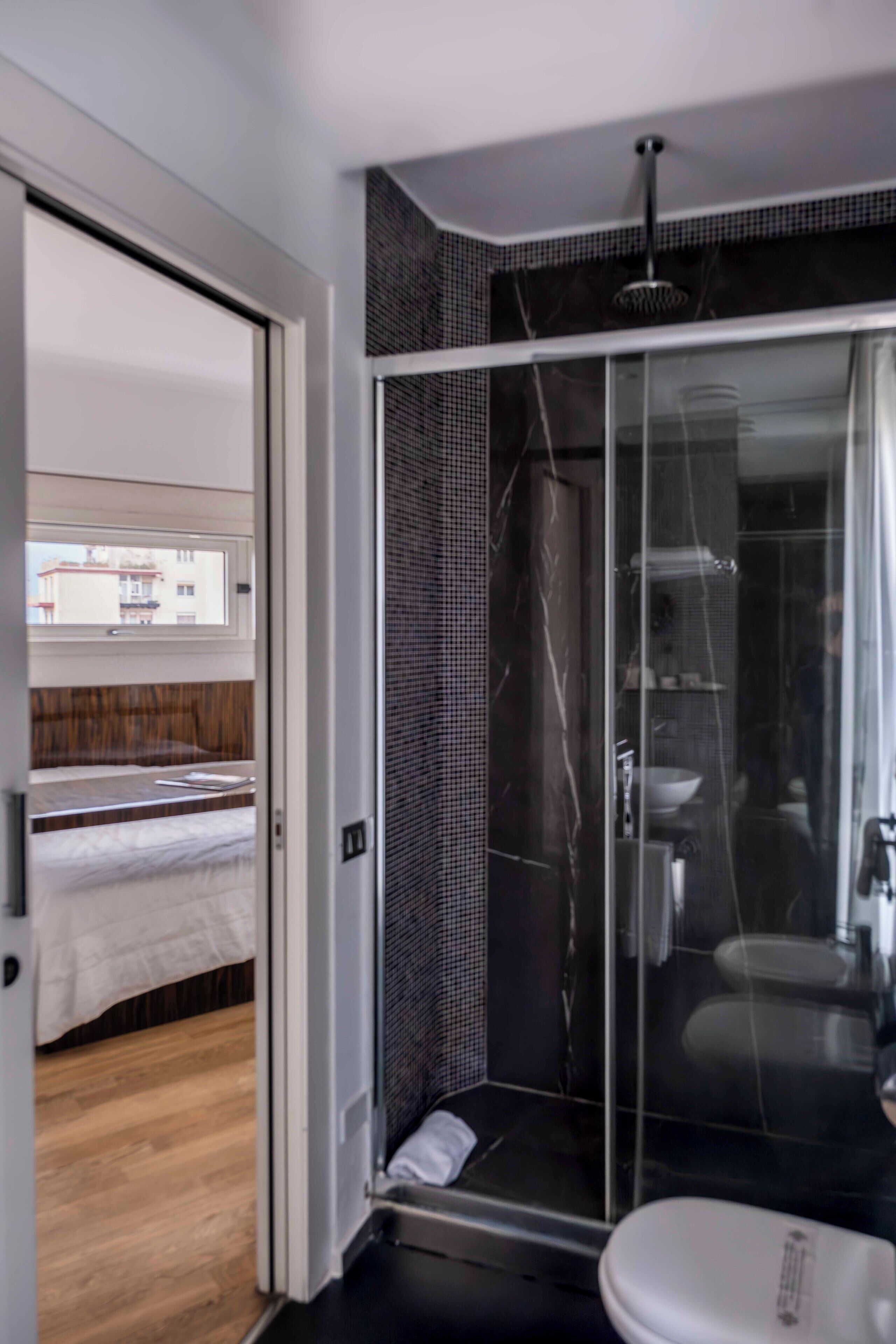 A modern bathroom with a glass shower enclosure, a white toilet, and a wooden floor.