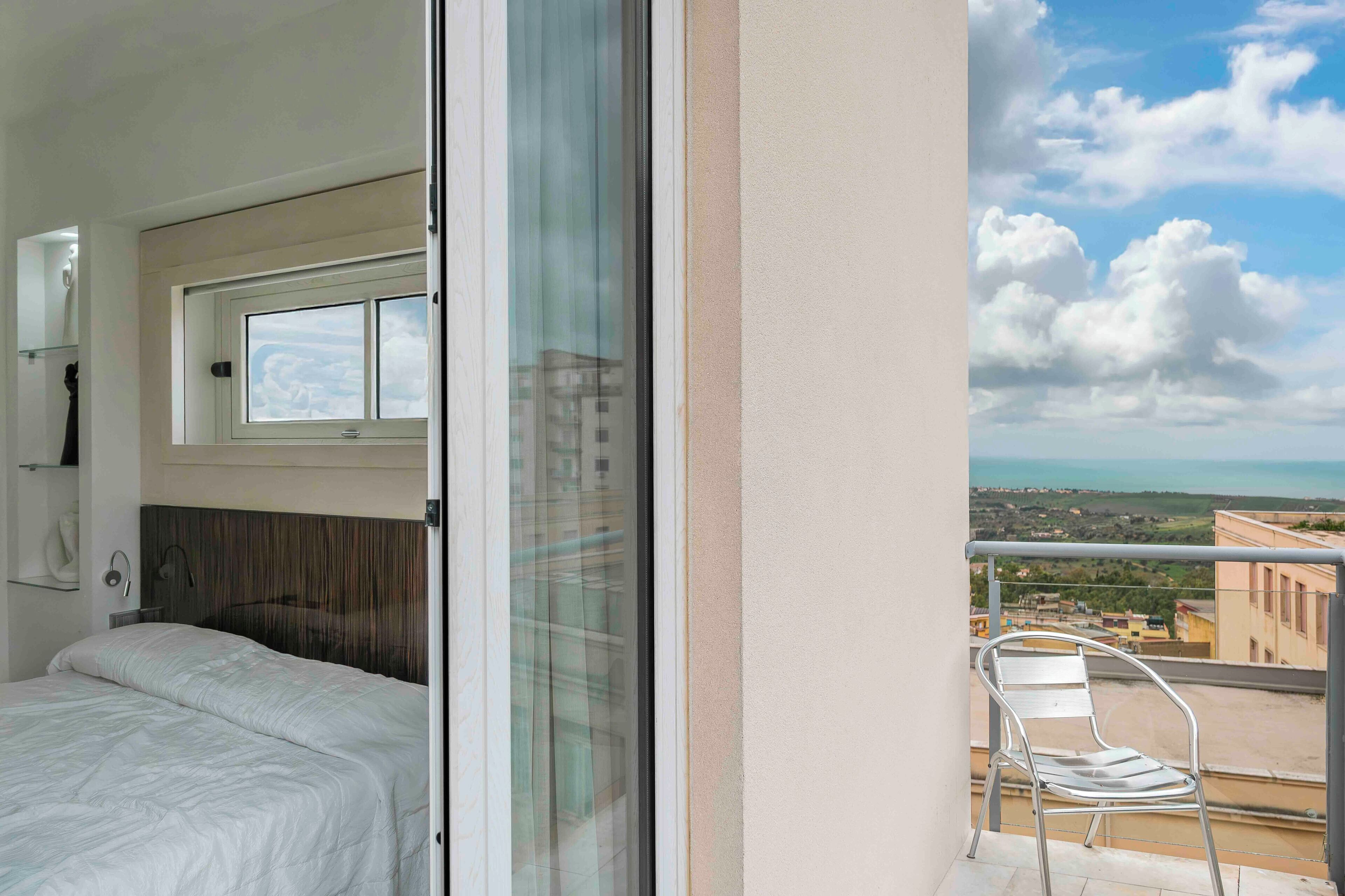 A bedroom with a bed, a window, and a balcony with a chair.