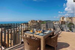 A balcony with wicker furniture, a table set for dining, and a cityscape view.