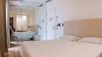 Una habitación de hotel moderna con una cama grande, un escritorio pequeño, una silla, un espejo y un armario.