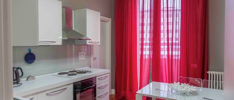 A modern kitchen with white cabinetry, a built-in oven, and a dining area with a white table and chairs.