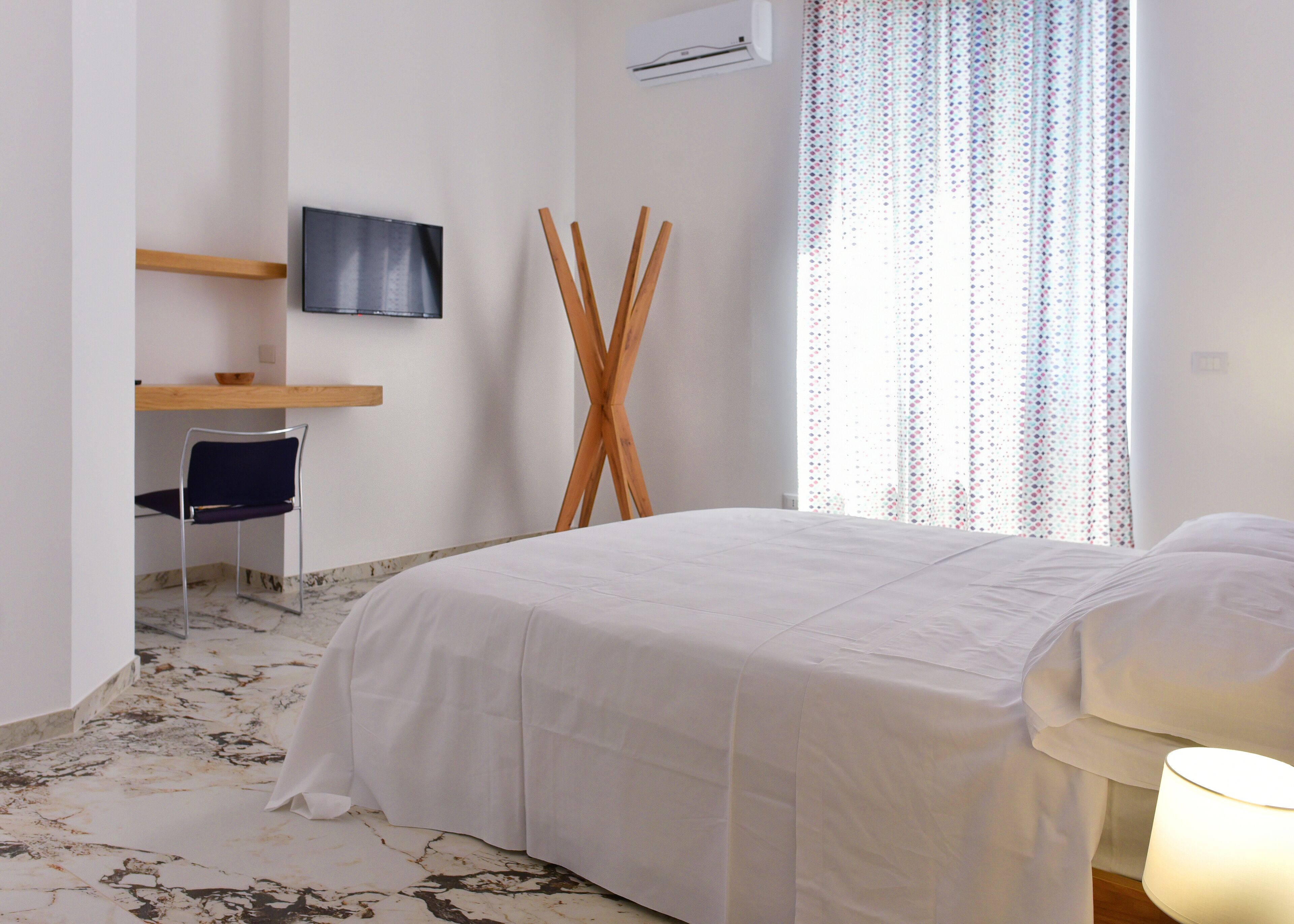 Una habitación de hotel con cama, escritorio y silla, televisor y ventana con cortinas.