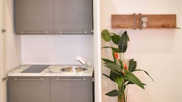 Una cocina compacta con armarios grises, un lavamanos de acero inoxidable y una encimera de mármol.
