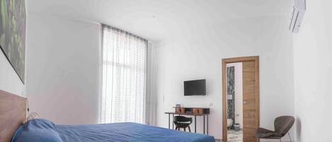 A bedroom with a bed, a desk with a chair, a television, and a bathroom door.