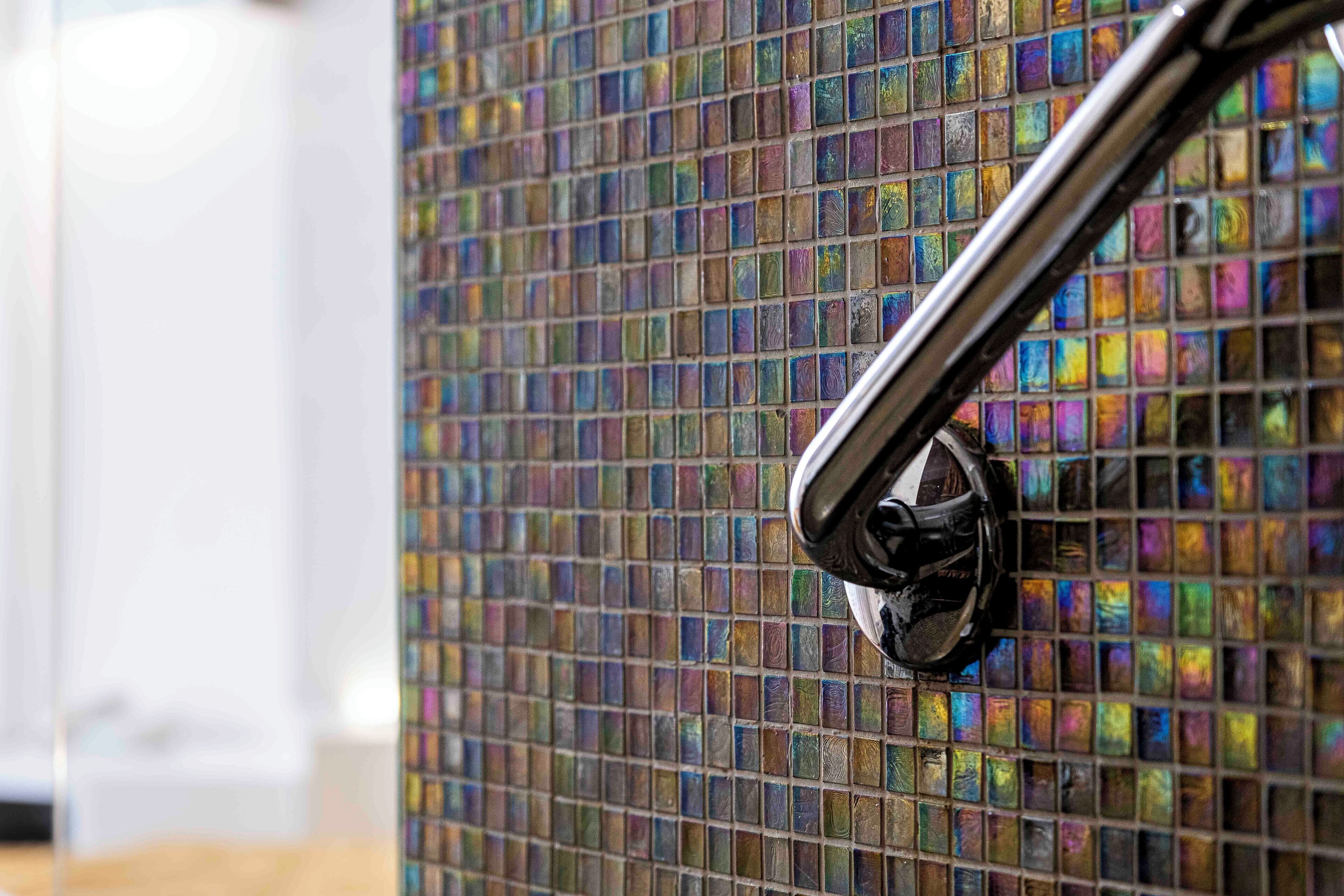 A bathroom with a tiled wall and a chrome faucet.