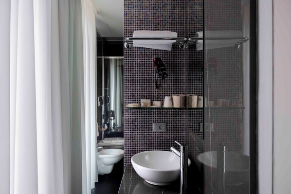 A modern bathroom with a large white sink, a glass shower enclosure, and a tiled backsplash.