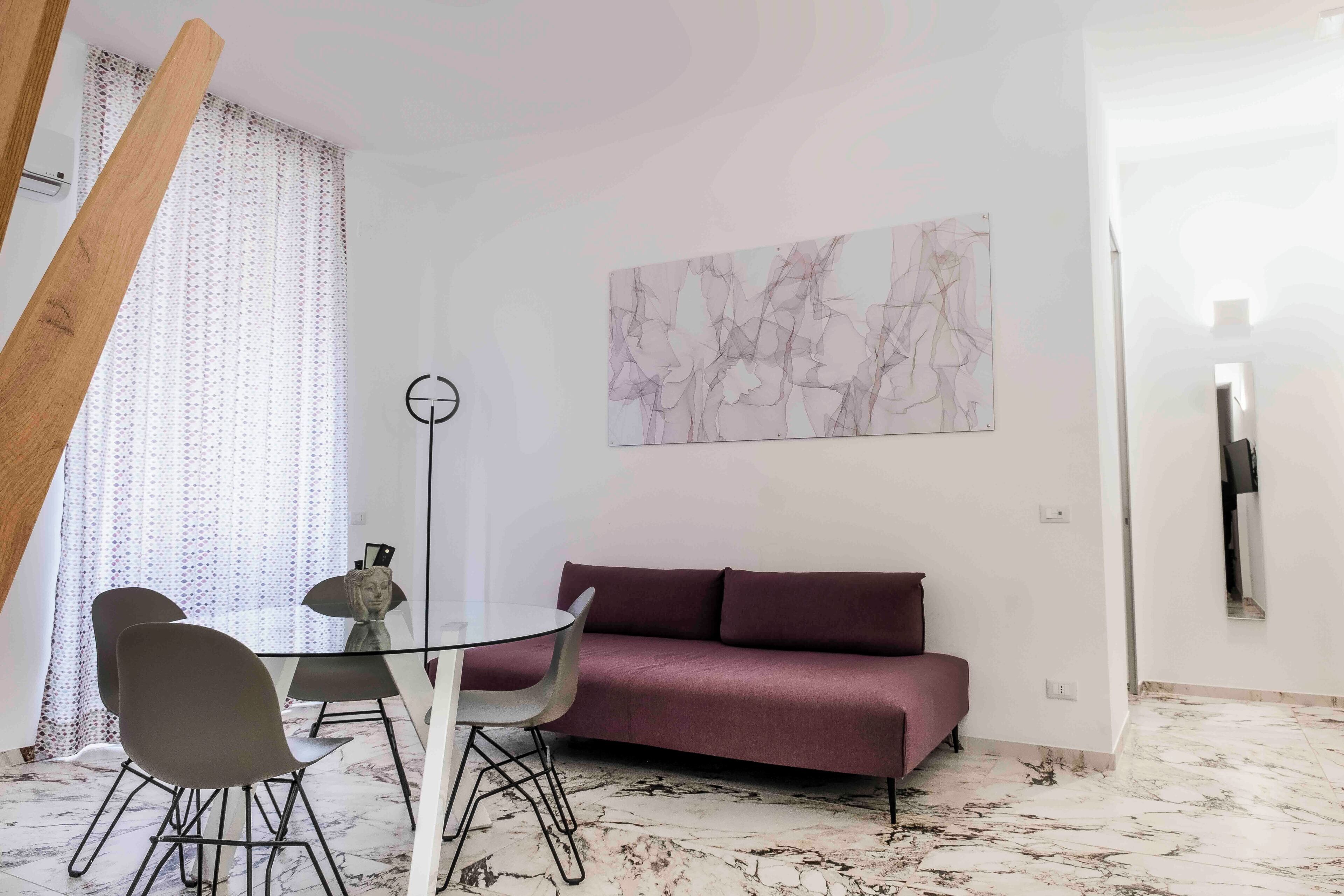 A modern living room with a glass dining table, two chairs, a purple sofa, and a marble floor.