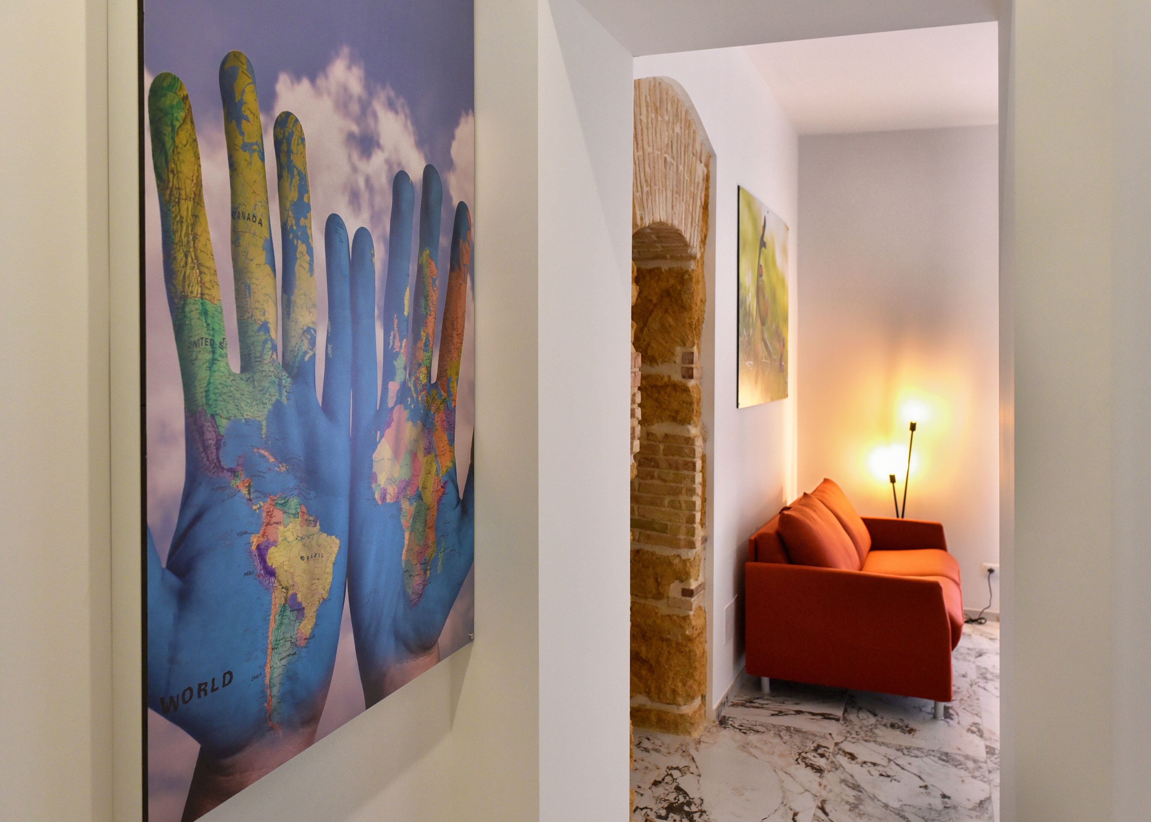 A room with a large world map mural, a brick wall, a red sofa, and a floor lamp.