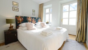 A neatly made bed with white linens and pink pillows, a bedside lamp, and a floral headboard. - Crystal Suites Chez Helena (Kraków)
