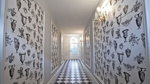 A hallway with patterned wallpaper and a checkered floor, leading to a door with a chandelier. - Crystal Suites Chez Helena (Kraków)