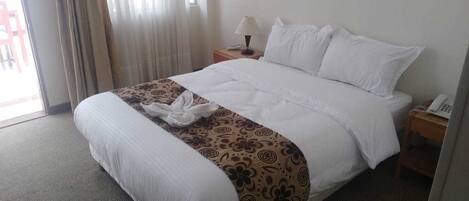 Una camera d'albergo con un letto, un comodino con una lampada, un telefono e una finestra con tende.