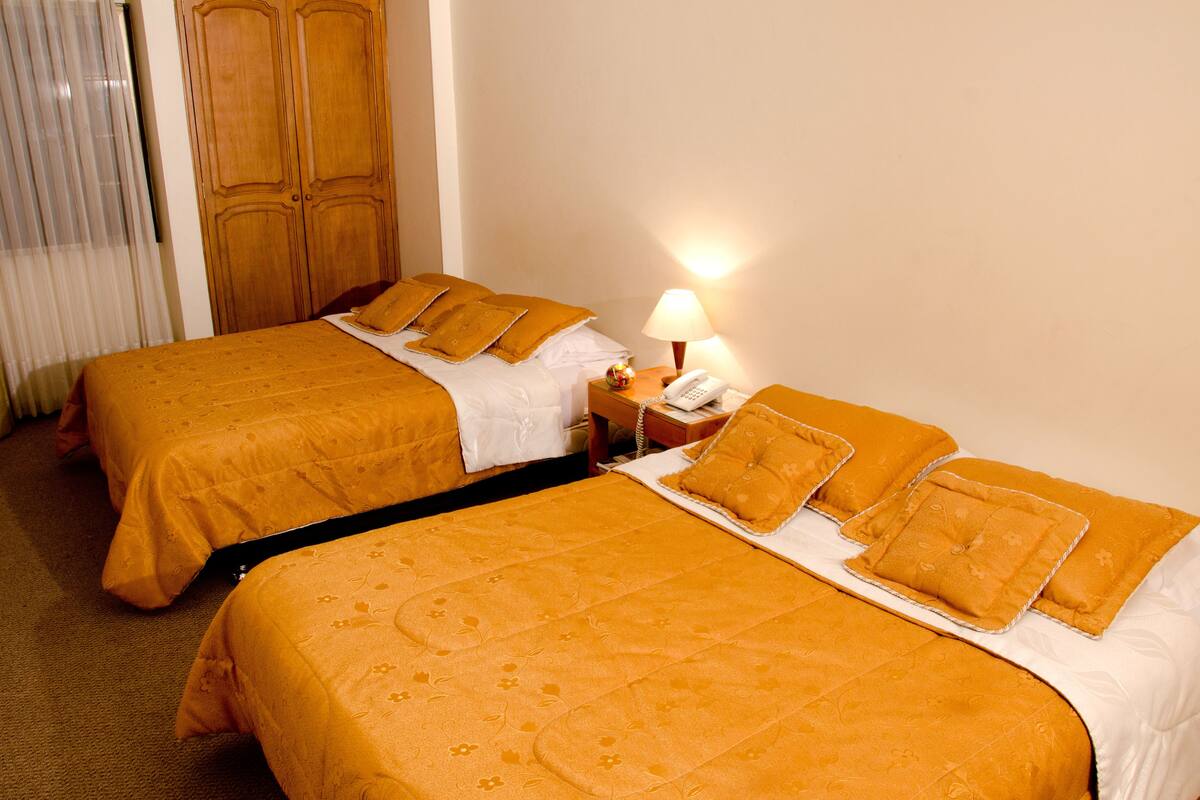Two single beds with matching orange bedding, a bedside table with a lamp, and a wooden wardrobe.