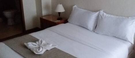 A hotel room with a neatly made bed, a bedside lamp, and a towel on the bed.