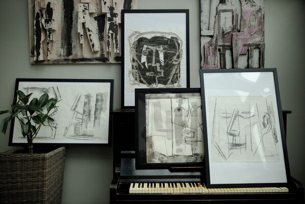 Une pièce avec un piano, des œuvres d’art encadrées accrochées au mur et une plante en pot.