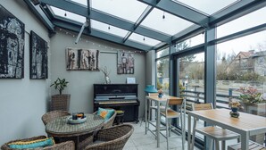 A conservatory with a piano, wicker furniture, and artwork on the walls. - Hotel Beethoven (Gdansk)
