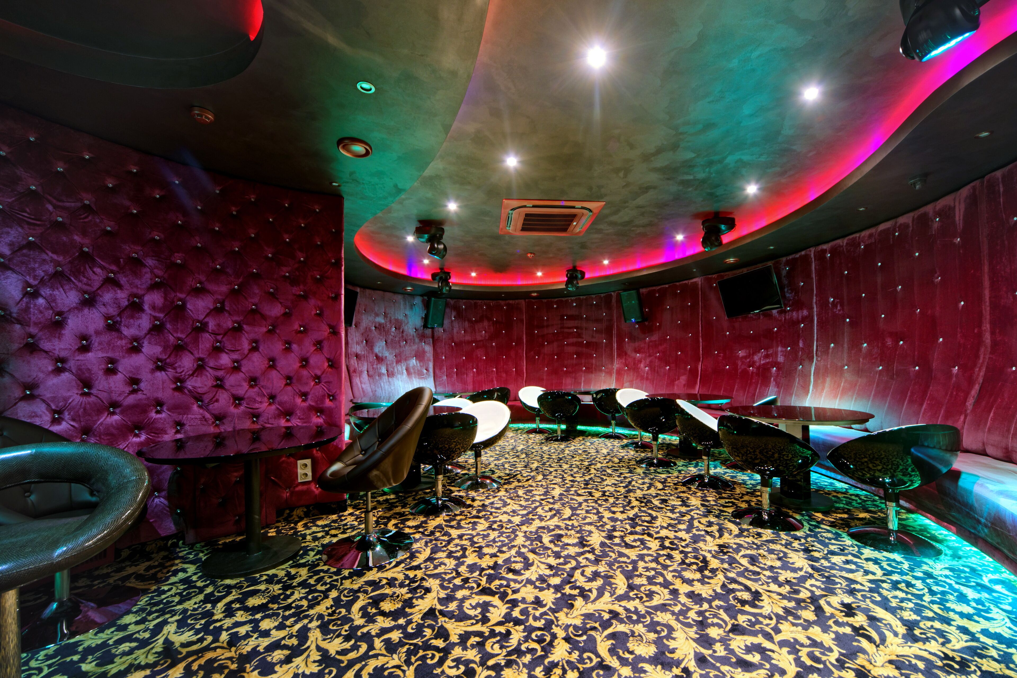 A room with a patterned carpet, red upholstered walls, and multiple chairs.