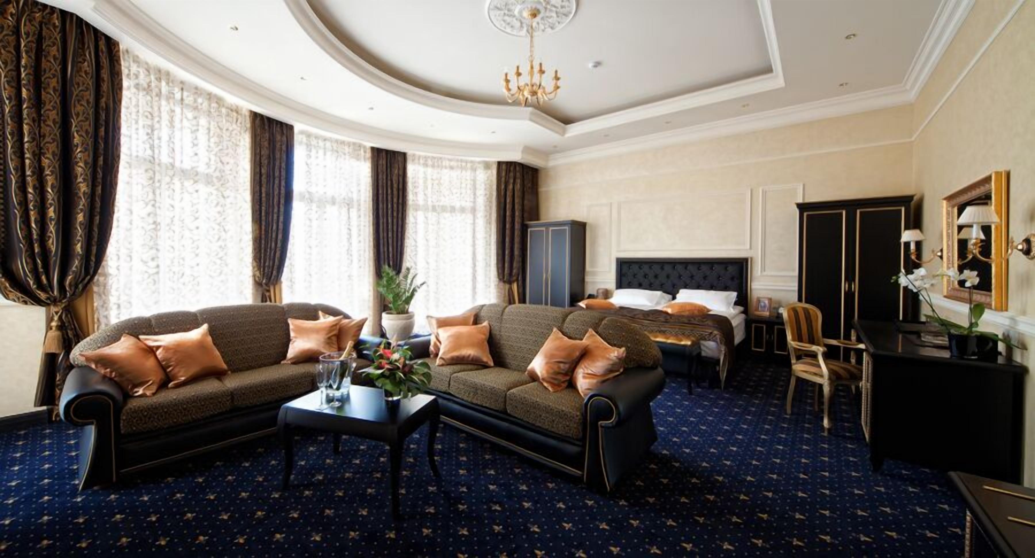 A hotel room with a dark blue carpet, two sofas, a bed, a desk, and a chandelier.