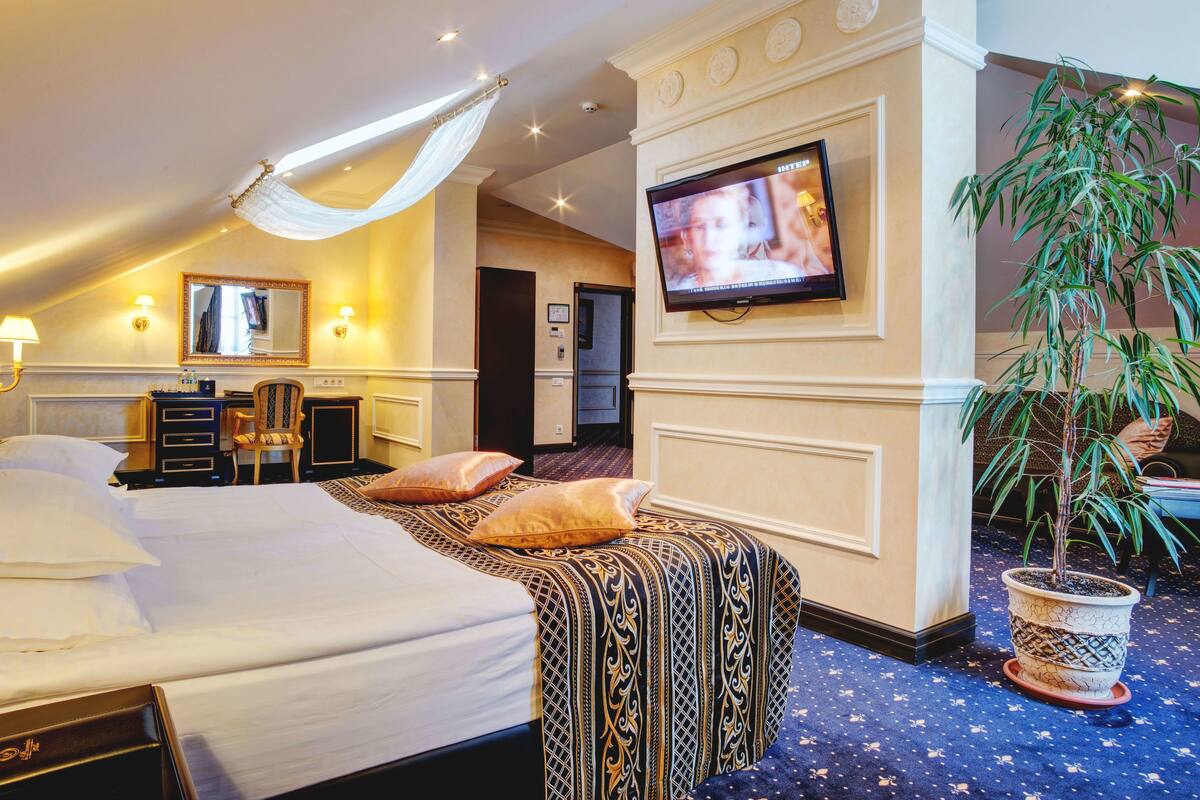 Una habitación de hotel con una cama grande, un escritorio, una silla, un televisor y una planta en maceta.