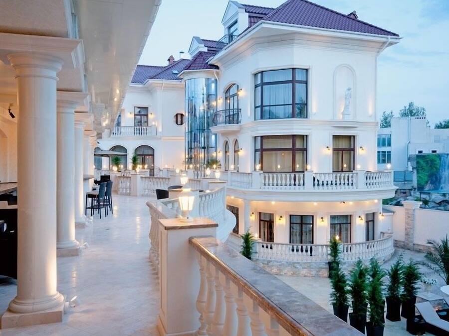 Een luxe hotel met een ruime buitenruimte, voorzien van sierlijke kolommen, meerdere eettafels en een goed verlicht balkon.