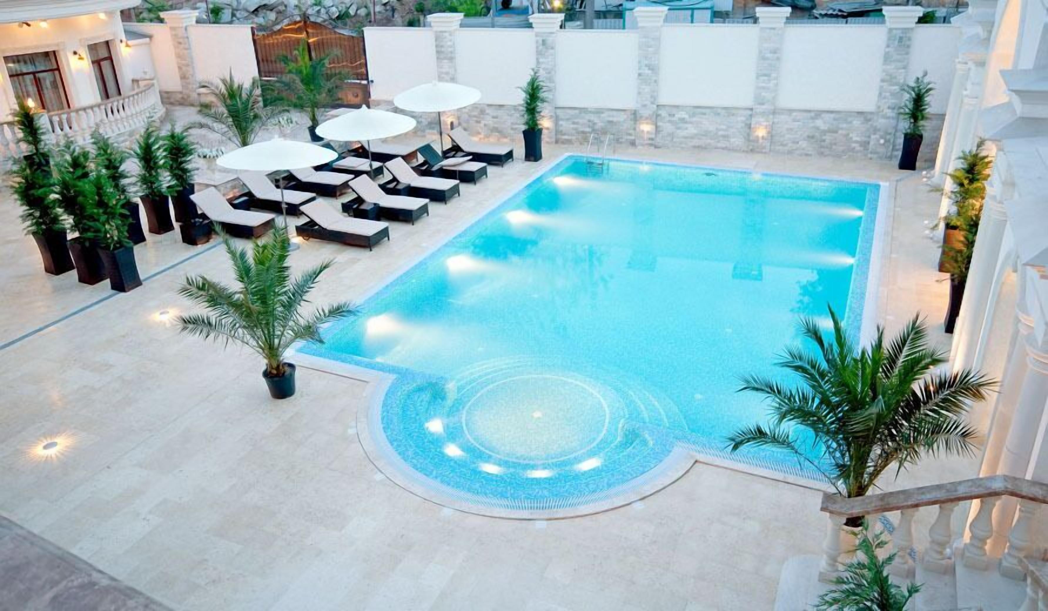 A rooftop pool with lounge chairs and umbrellas, surrounded by potted plants and a stone wall.