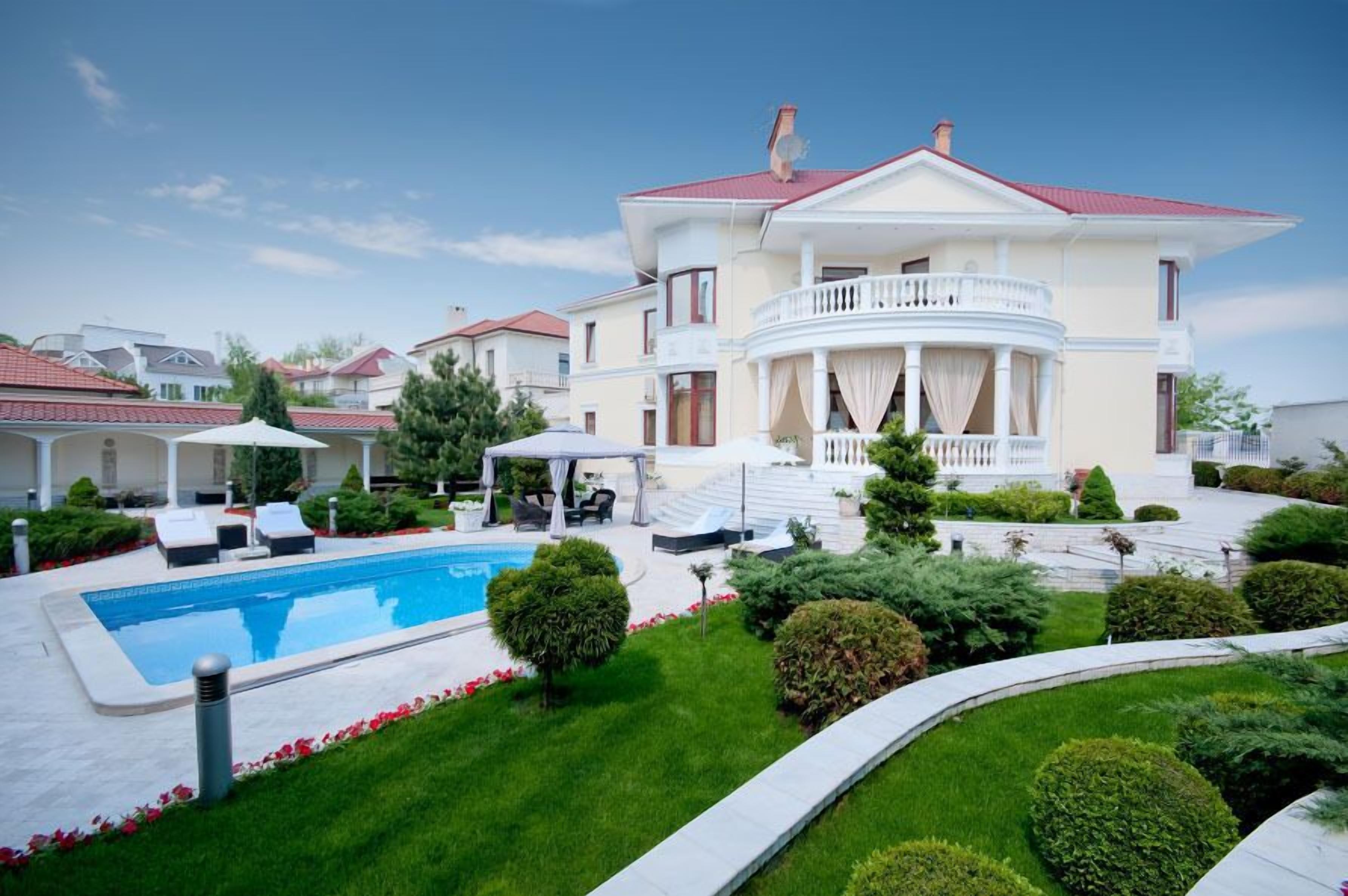 A large, two-story house with a swimming pool, a covered patio, and well-maintained gardens.