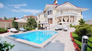 Una casa grande con piscina, mobiliario exterior y un jardín bien cuidado.