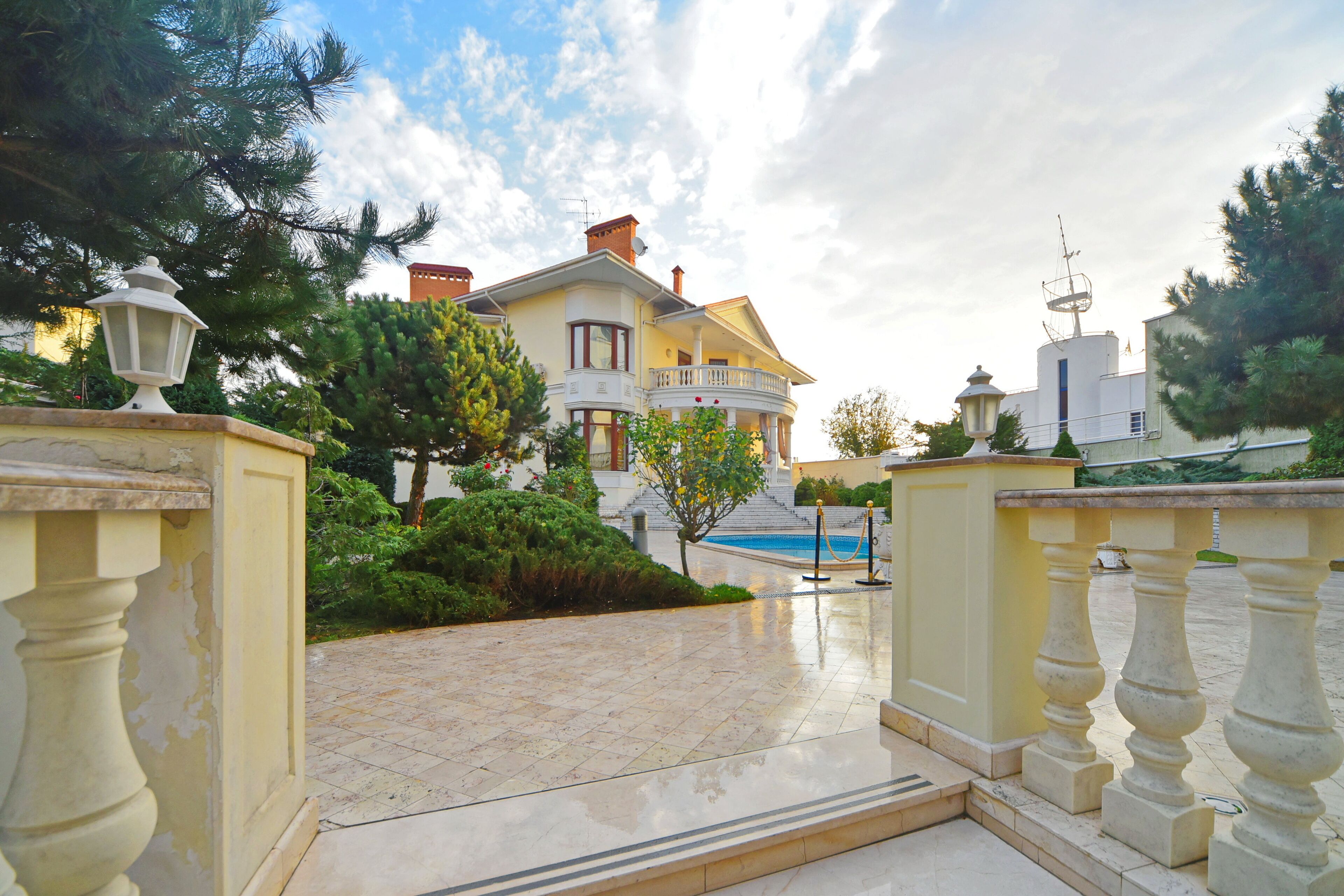 A large, two-story house with a balcony, surrounded by greenery and a swimming pool.