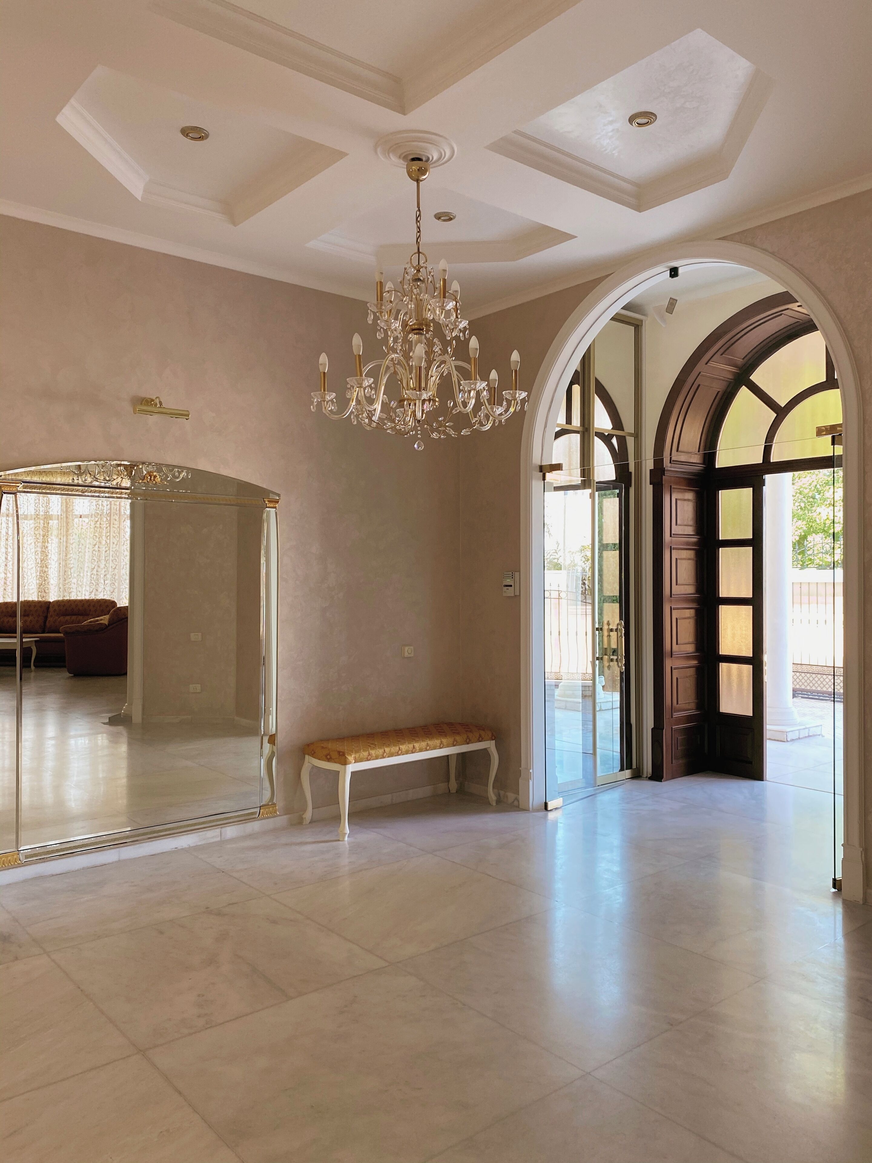 A spacious room with a large mirror, a bench, and a chandelier.