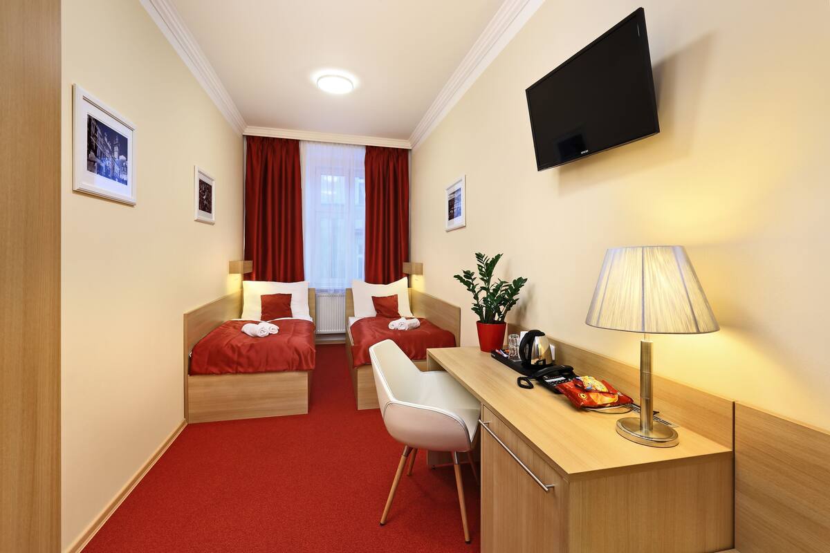 Une chambre d’hôtel avec deux lits, un bureau, une chaise, une télévision et une plante.