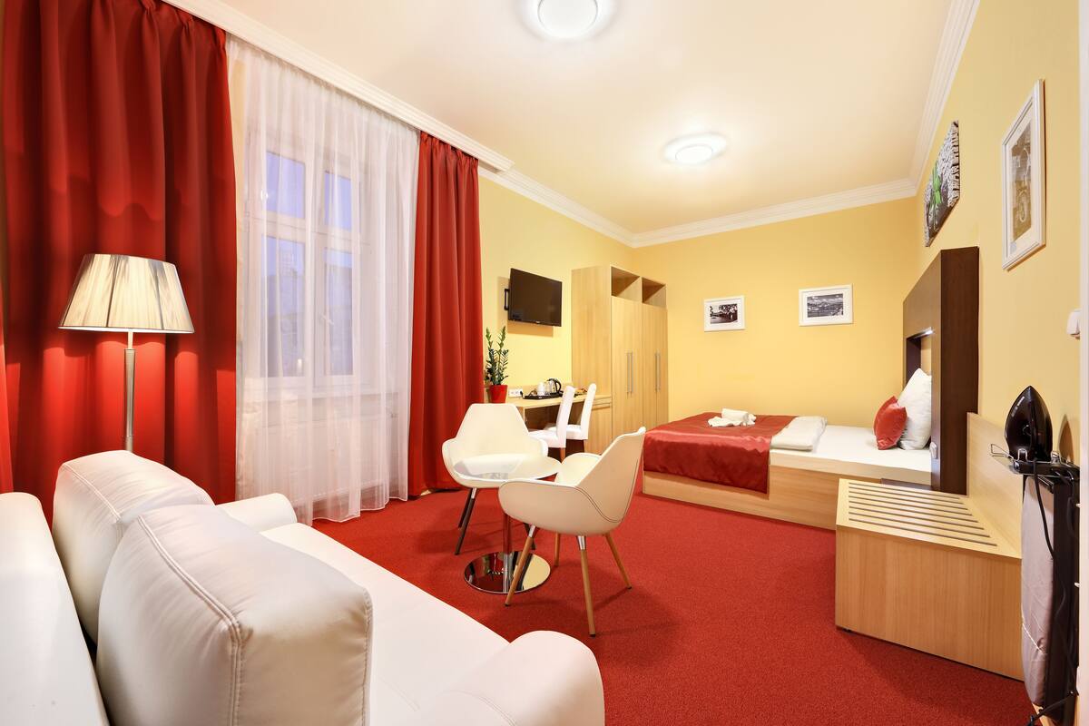 Une chambre d’hôtel avec un tapis rouge, un canapé, un bureau, une chaise, un lit et un téléviseur.